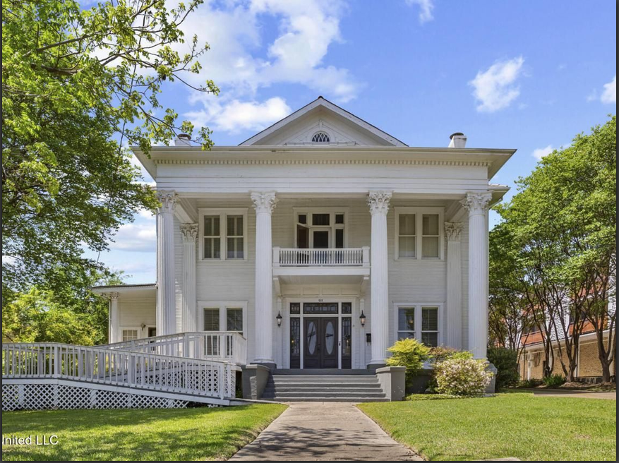 A large white building with columns, flanked by trees.